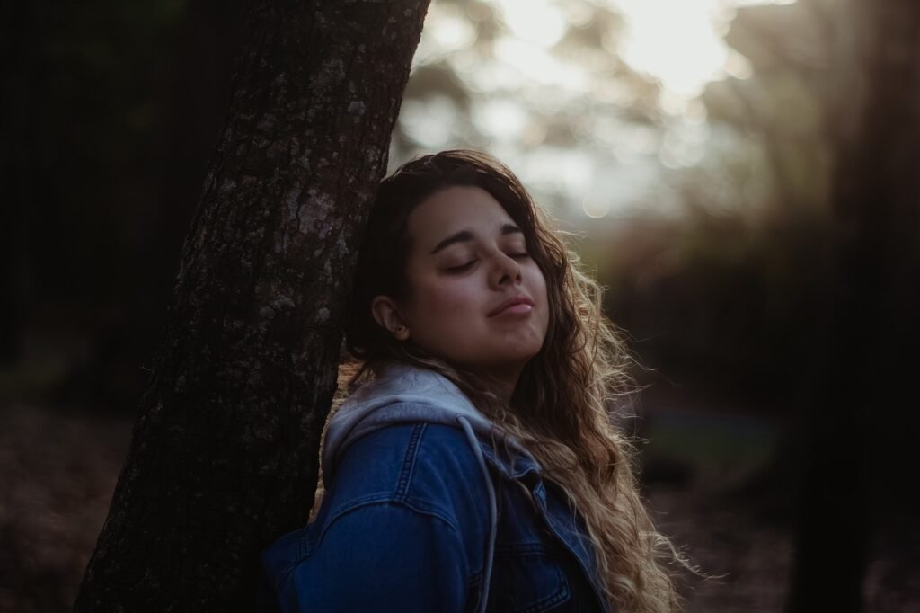 Jeune femme les yeux clos, adossée à un arbre dans une lumière dorée, image des états modifiés de conscience
